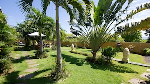 A well-maintained garden with a stone pathway, palm trees, and a statue. - Ocean Villa Dive Resort - Tulamben (Tulamben)