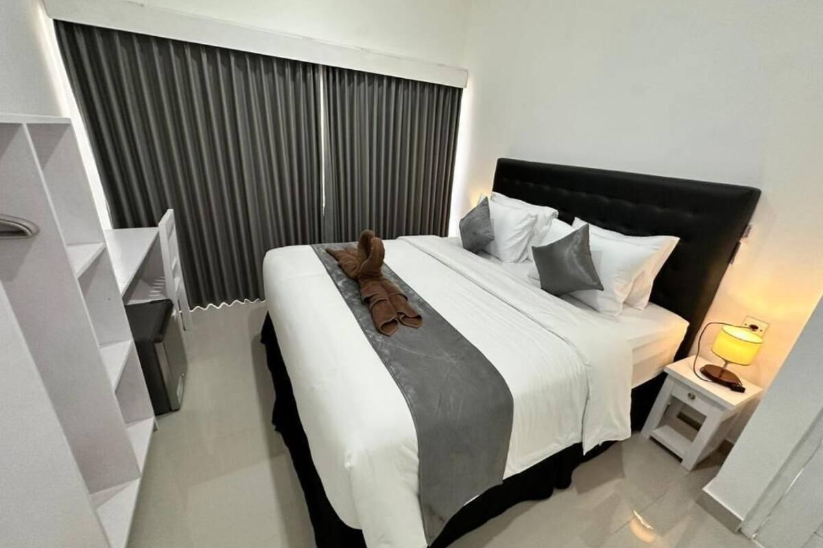 A neatly made bed with a black headboard, white bedding, and a grey accent. There is a bedside lamp on the right.