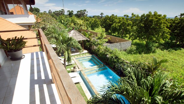 A swimming pool surrounded by lush greenery, a stone wall, and a thatched-roof structure. - Ocean Villa Dive Resort - Tulamben (Tulamben)