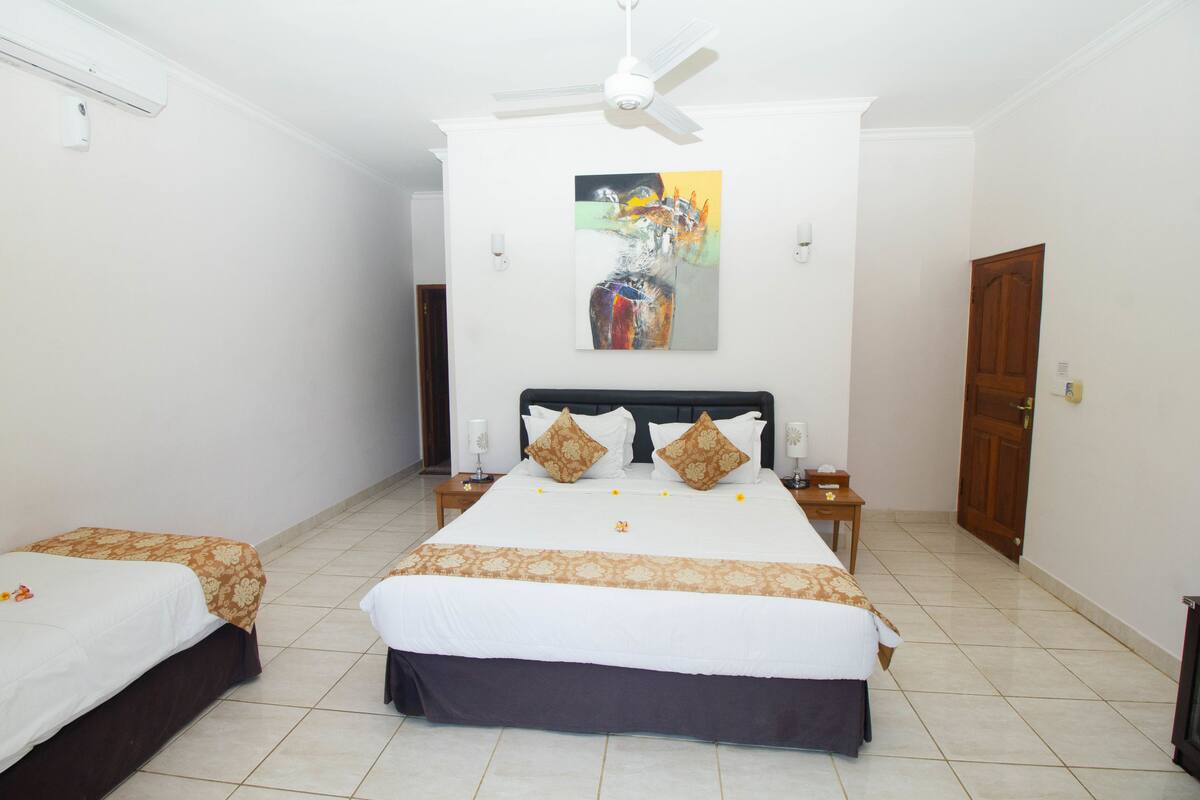 A hotel room with a large bed, two bedside tables, a ceiling fan, and a painting on the wall.