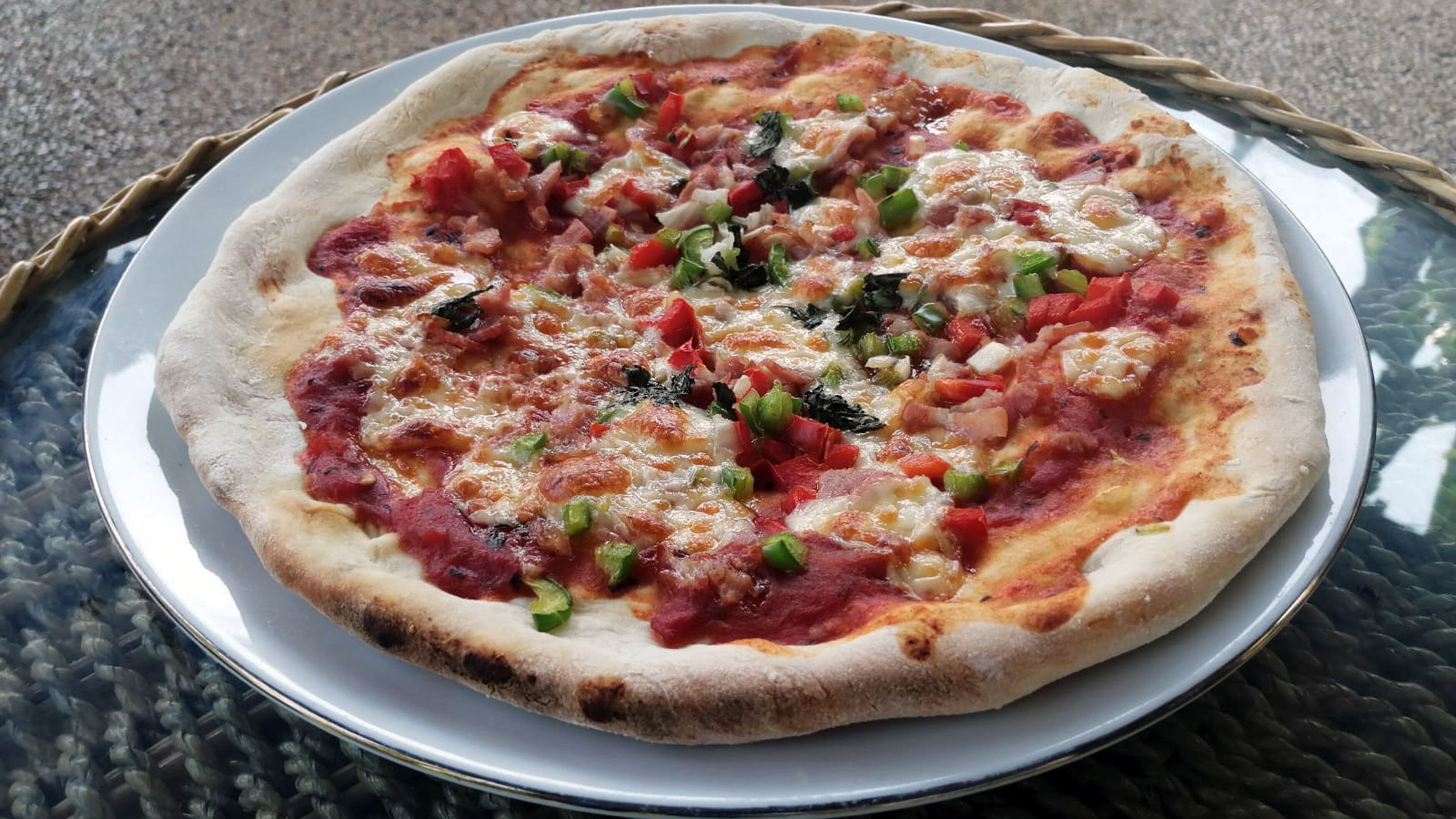 A pizza on a metal plate with a woven basket underneath.