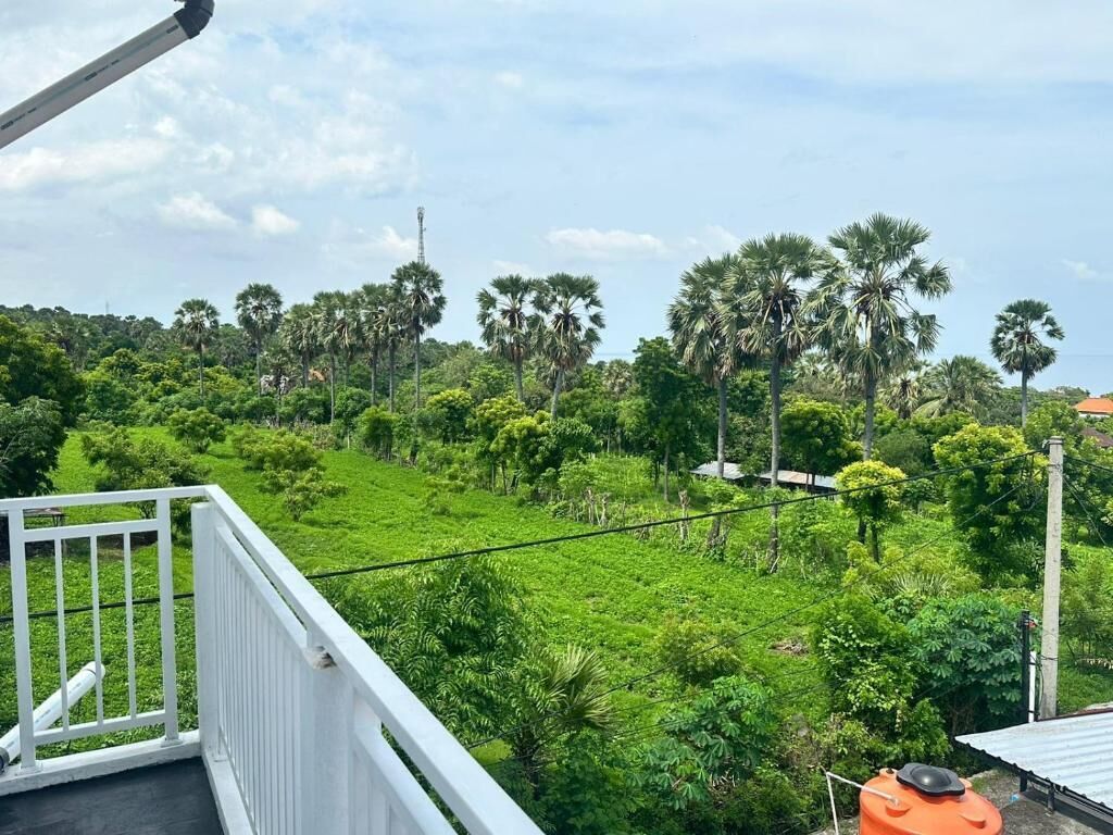 Un balcon offrant une vue sur un paysage verdoyant et luxuriant, avec des palmiers et une tour visible au loin.