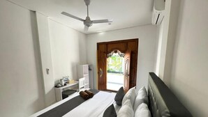 A hotel room with a bed, a desk, a chair, a ceiling fan, and a window with a view of greenery. - Ocean Villa Dive Resort - Tulamben (Tulamben)