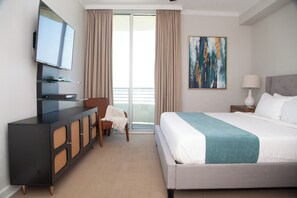 Hotelkamer met een groot bed, een aan de muur bevestigde televisie, een stoel, een schilderij en een balkon met gordijnen.
