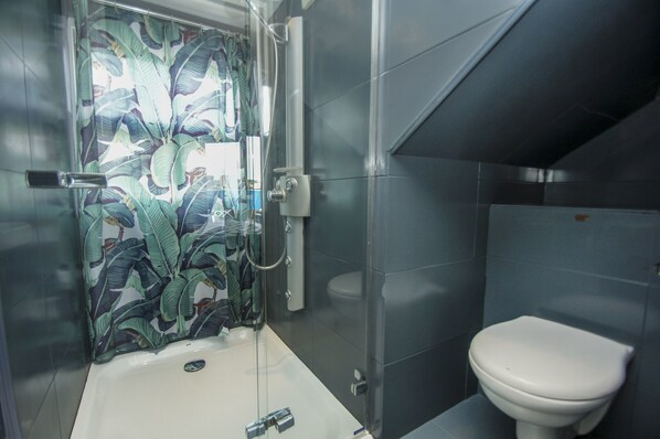 Un baño con ducha, inodoro y cabina de ducha de vidrio con diseño de hojas de plátano.