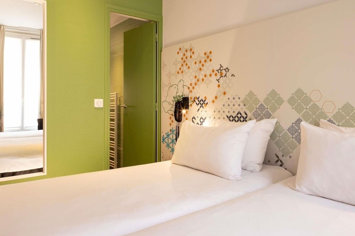 A hotel room with a bed, a green door, and a wall with geometric patterns.