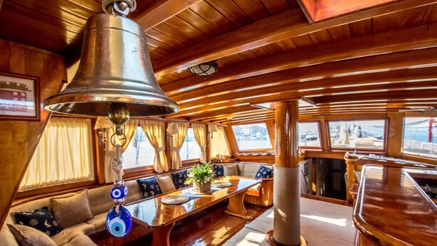 A cabin with a wooden interior, a large bell, a sofa with cushions, a table with a plant, and a cat tree. - Venezia Boat San Marco (Venice)