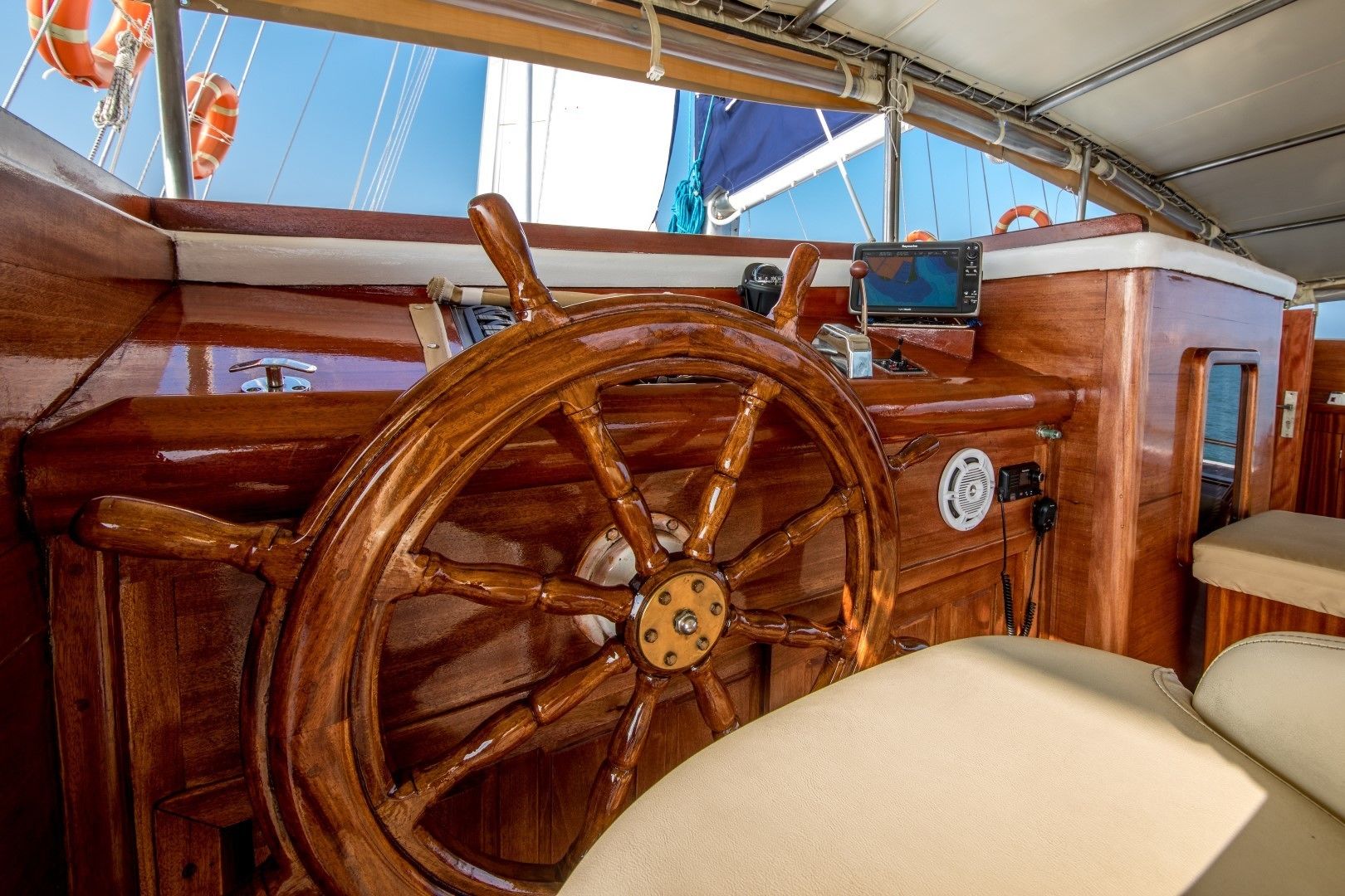 A wooden steering wheel, a control panel, and a cushioned seat on a boat deck.