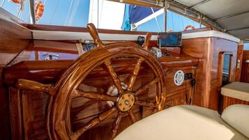 A wooden steering wheel, a control panel, and a cushioned seat on a boat deck.