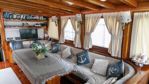 A cozy cabin interior with a sofa set, a table with a lace tablecloth, and a bookshelf filled with books and decorative items. - Venezia Boat San Marco (Venice)