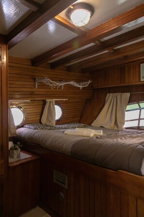 A cozy cabin-style bedroom with a bed, a window, and a small table with a plant. - Venezia Boat San Marco (Venice)