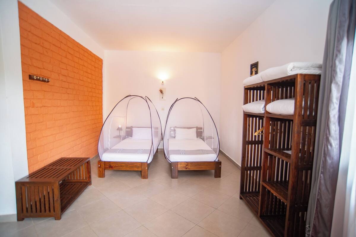 Een kamer met twee houten bedden met muggennetten, een houten bank en een houten kledingkast.