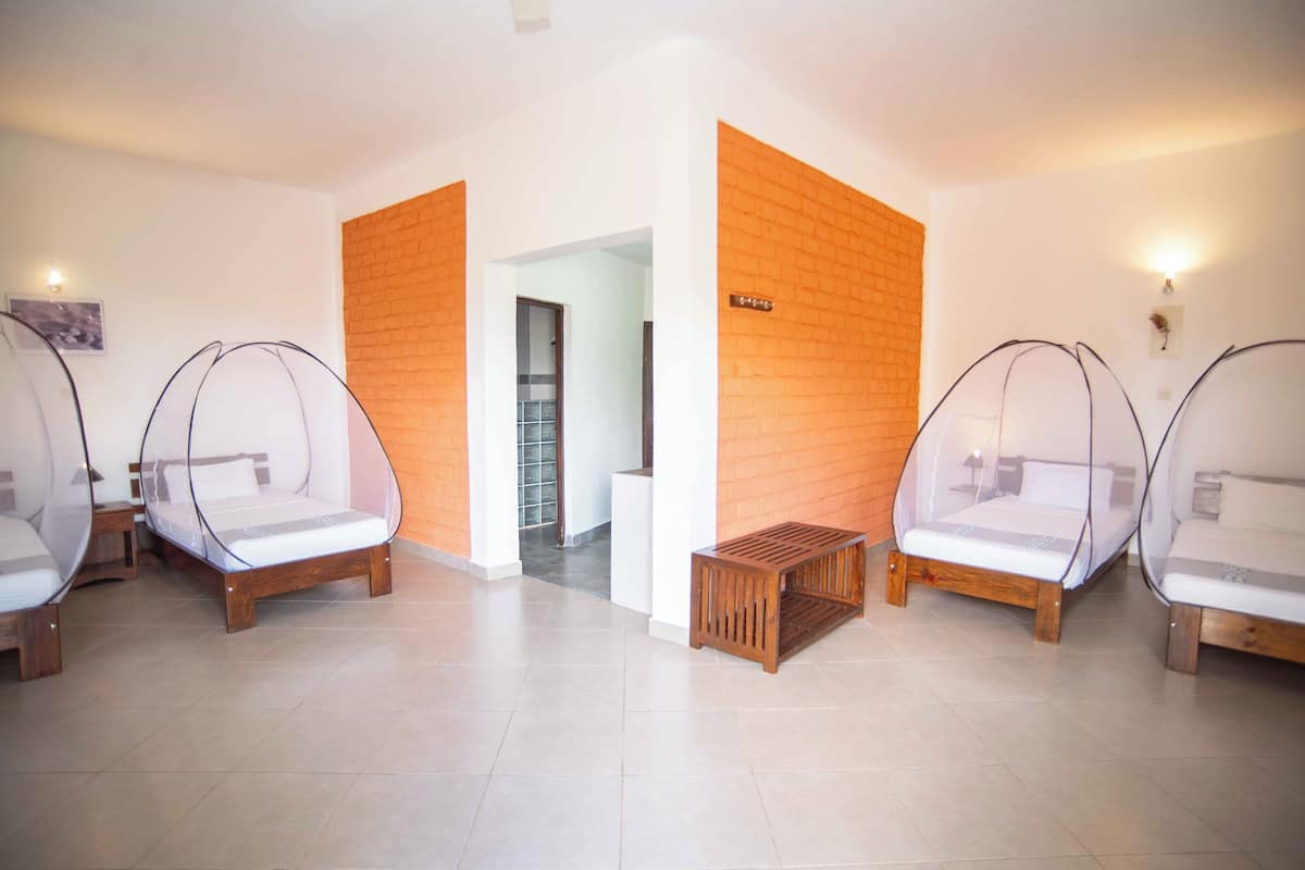 Een hotelkamer met vier bedden, elk voorzien van een hemelbed, en een houten bank in het midden.