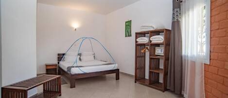 Un dormitorio con cama, mesita de noche, banco, armario y ventana con cortinas.