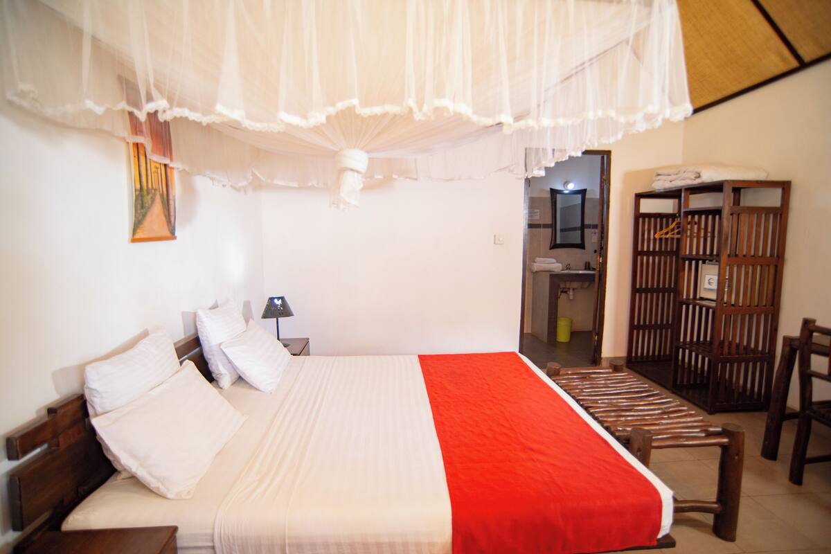 Een hotelkamer met een bed, nachtkastje, stoel, houten garderobe en spiegel.