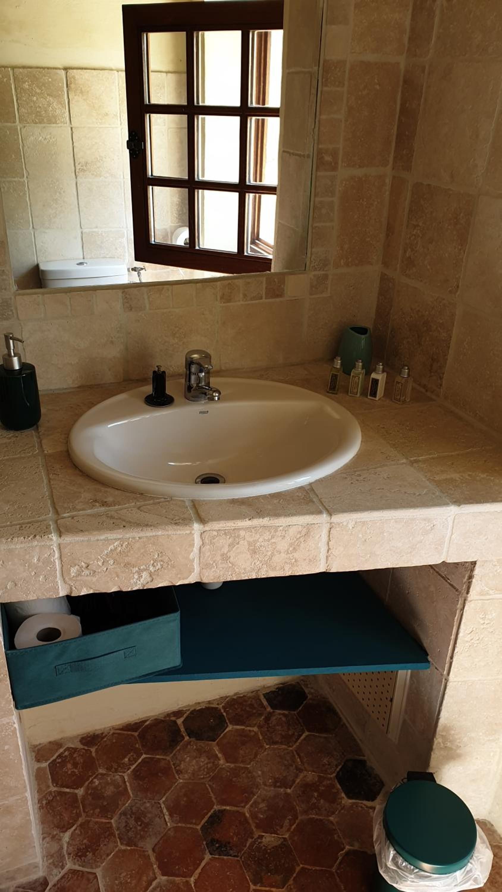 A bathroom with a white sink, a window above the sink, and a tiled floor.