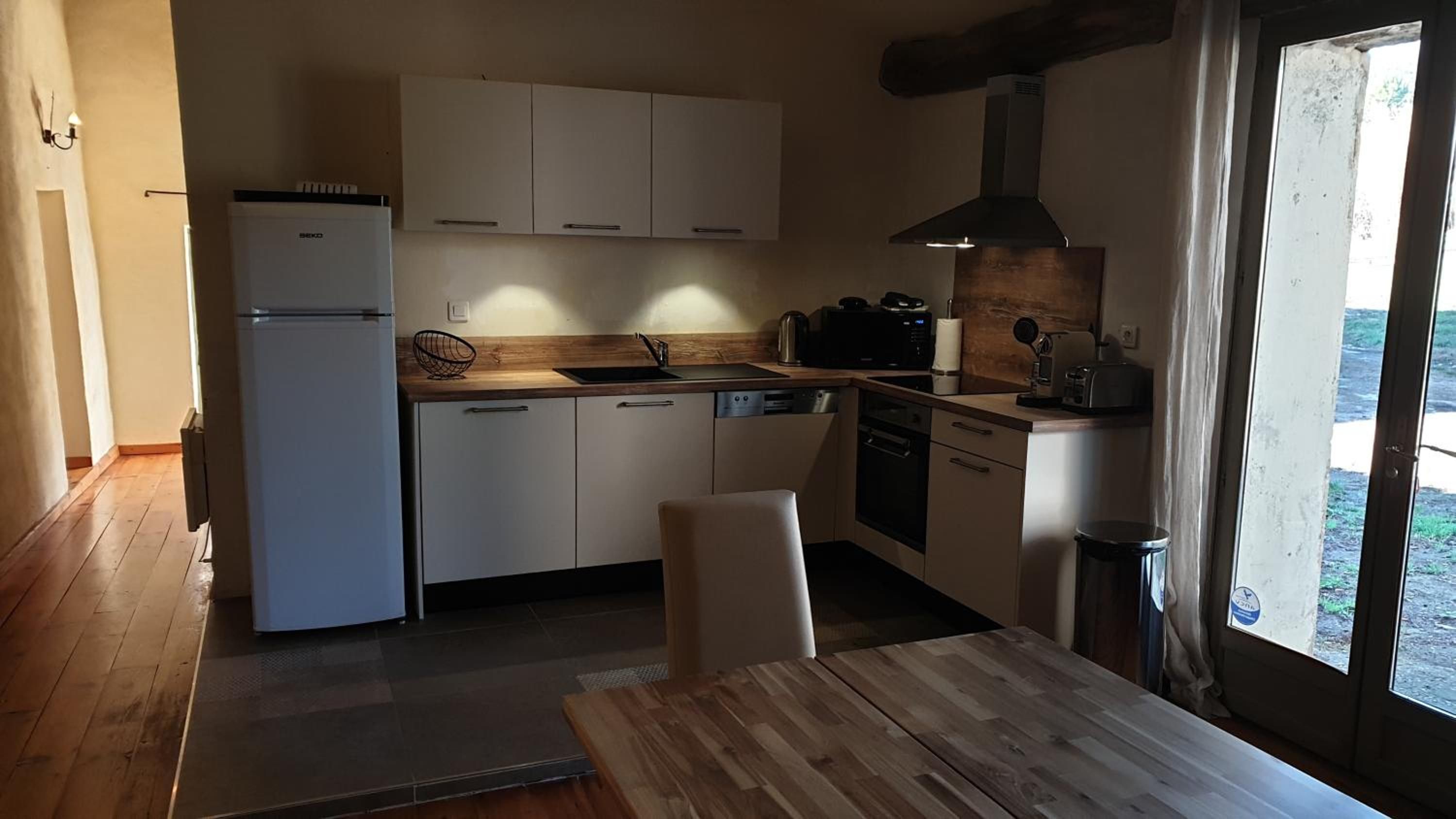 A compact kitchen with white cabinets, a built-in oven, a sink, and a window providing natural light.