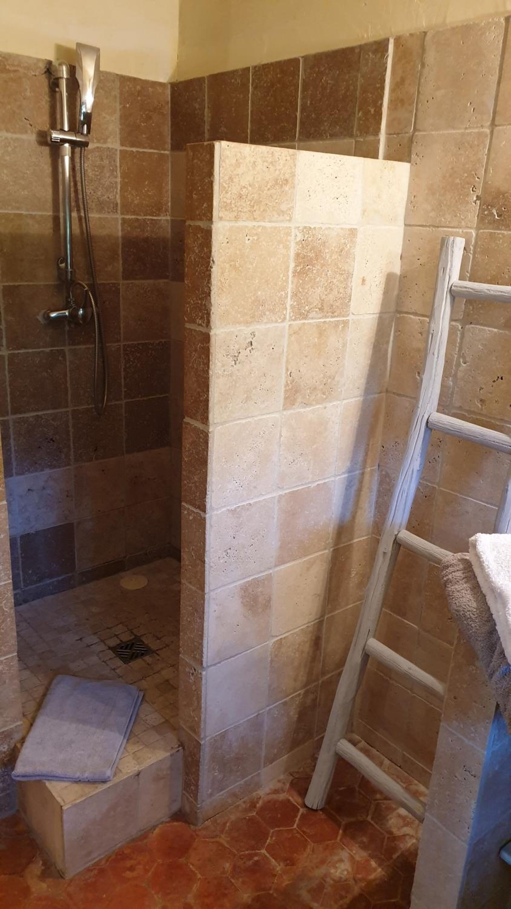 Un espace douche avec un mur carrelé, une pomme de douche et une échelle appuyée contre le mur.