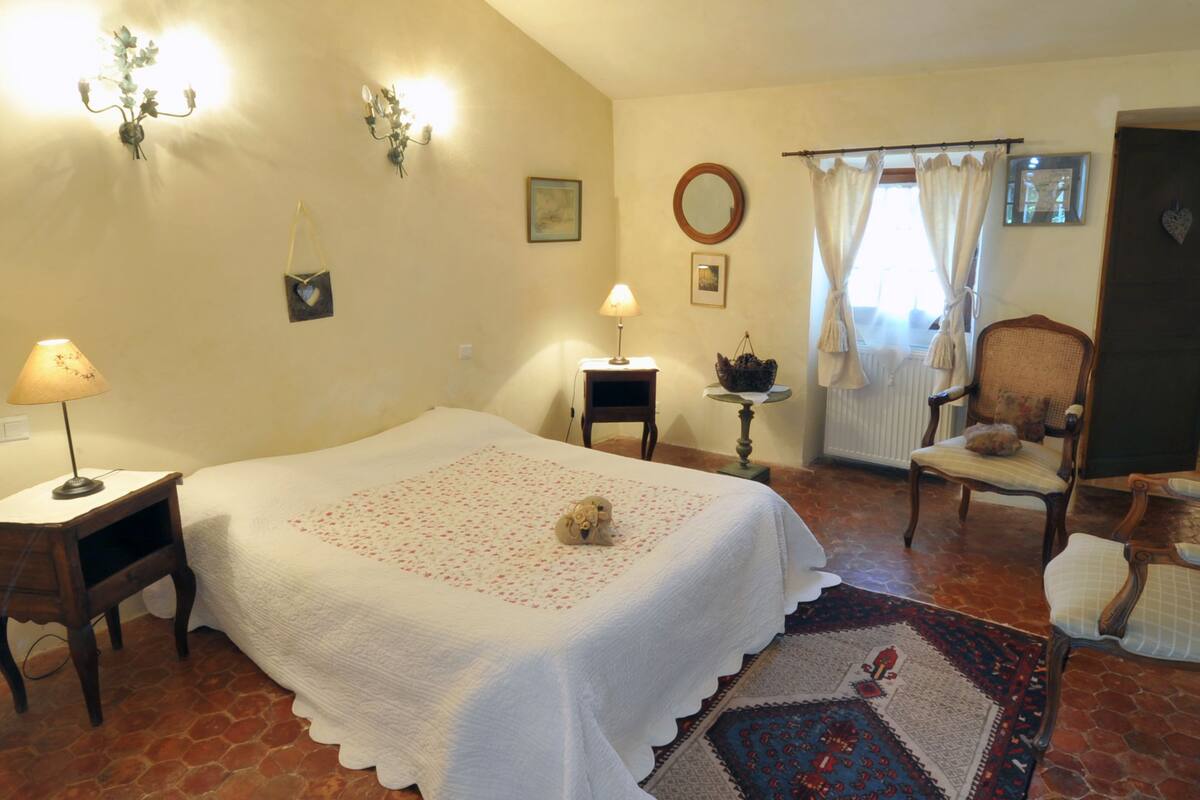 Un dormitorio acogedor con cama, una silla, una mesita y una lámpara.