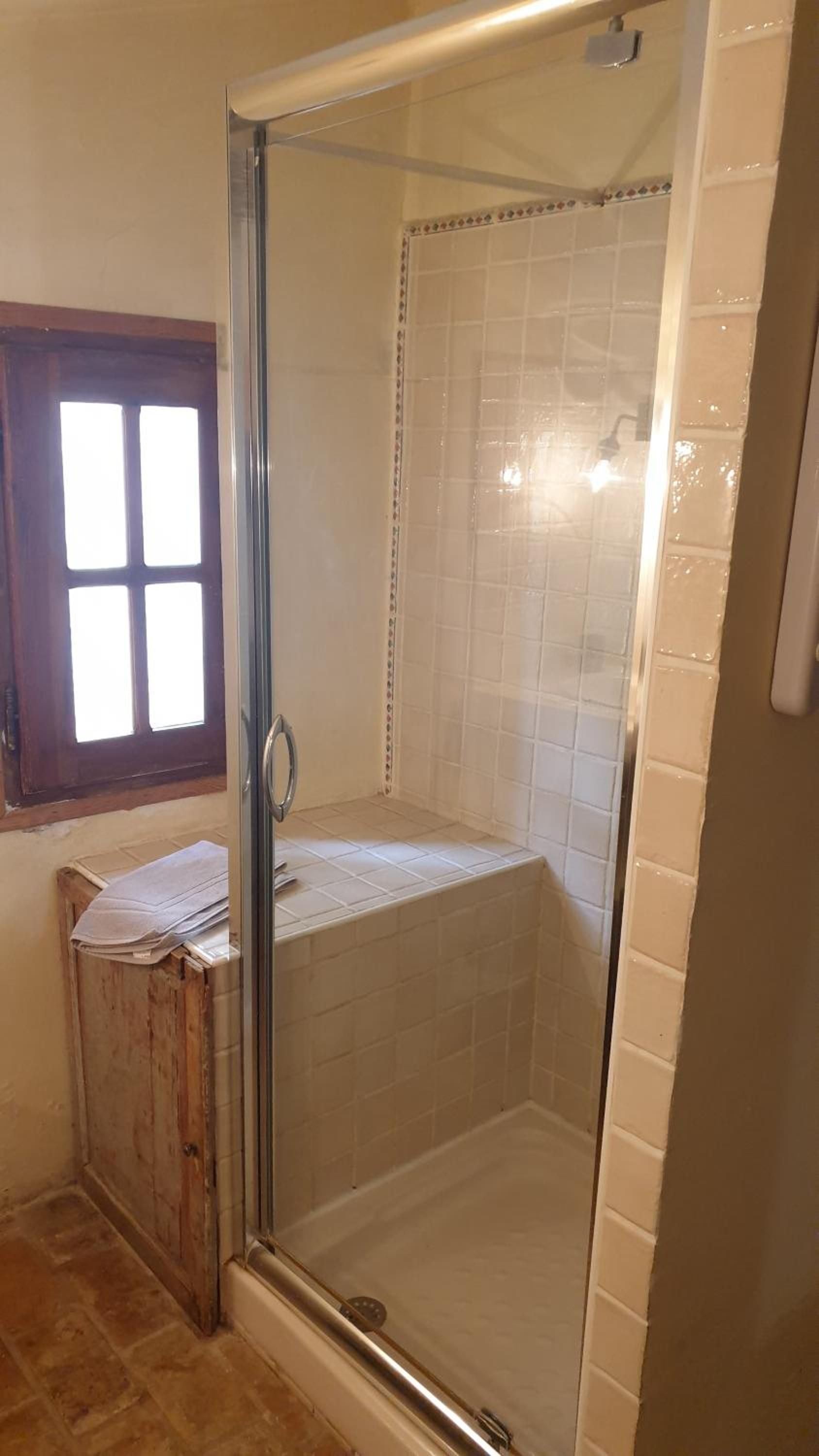 A glass-enclosed shower area with white tiles and a window above.
