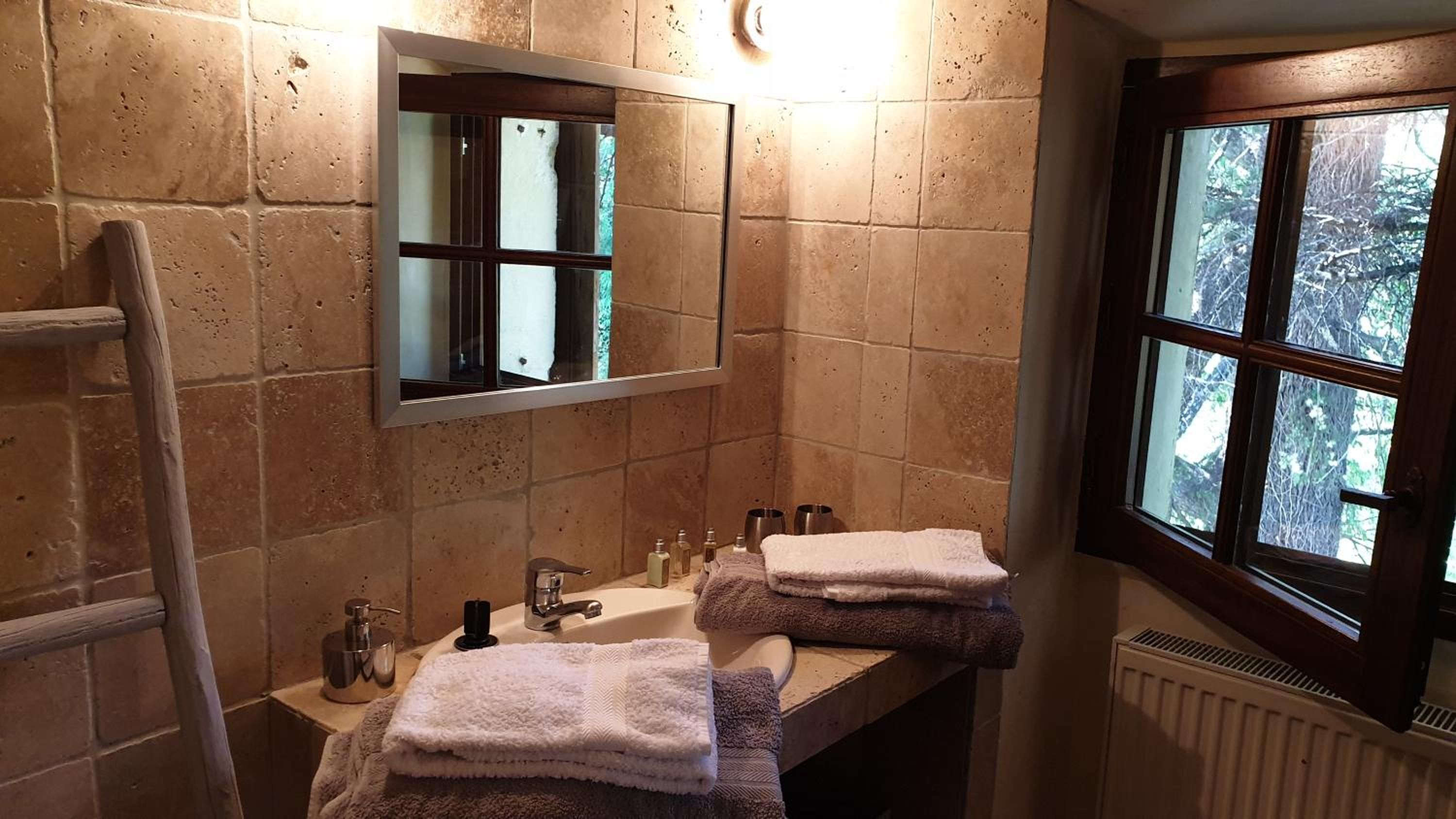 A bathroom with a wooden vanity, a mirror, a towel rack, and a window with a view of trees.