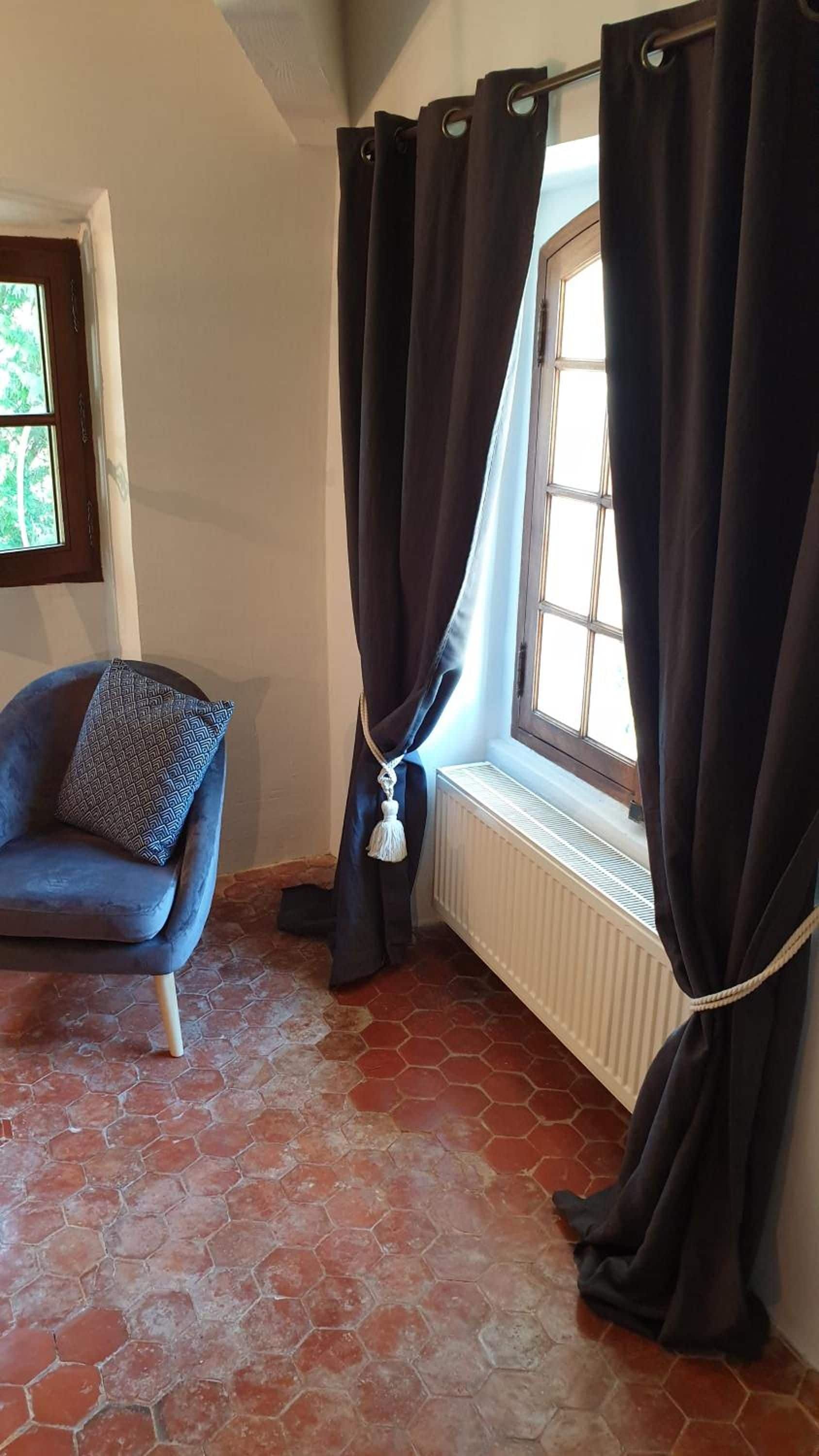 Een kamer met een blauwe stoel, een raam met gordijnen en een radiator.
