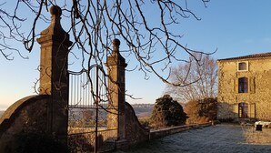 A stone building with a traditional facade, a metal gate, and a view of the countryside. - Bastide de l'Adrech (Manosque)