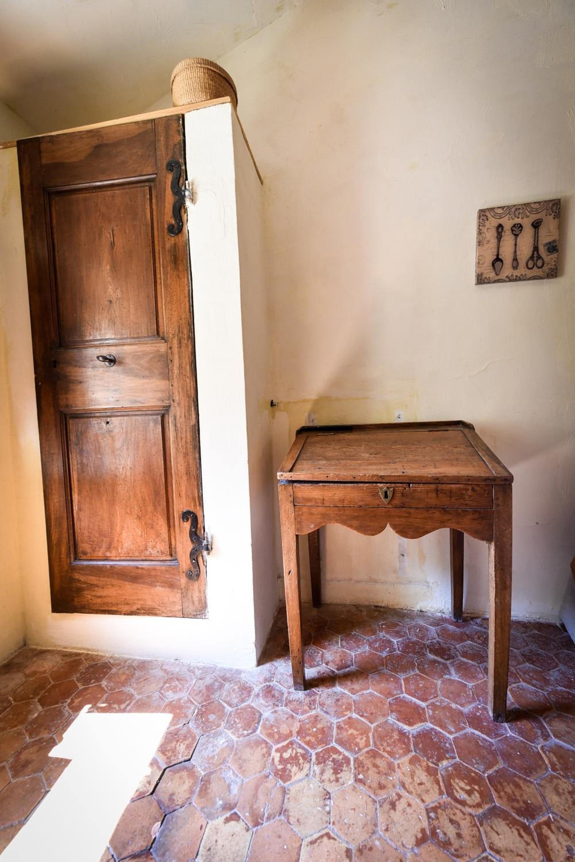 Une pièce rustique avec une porte en bois, une petite table en bois et un sol carrelé en forme d’hexagone.