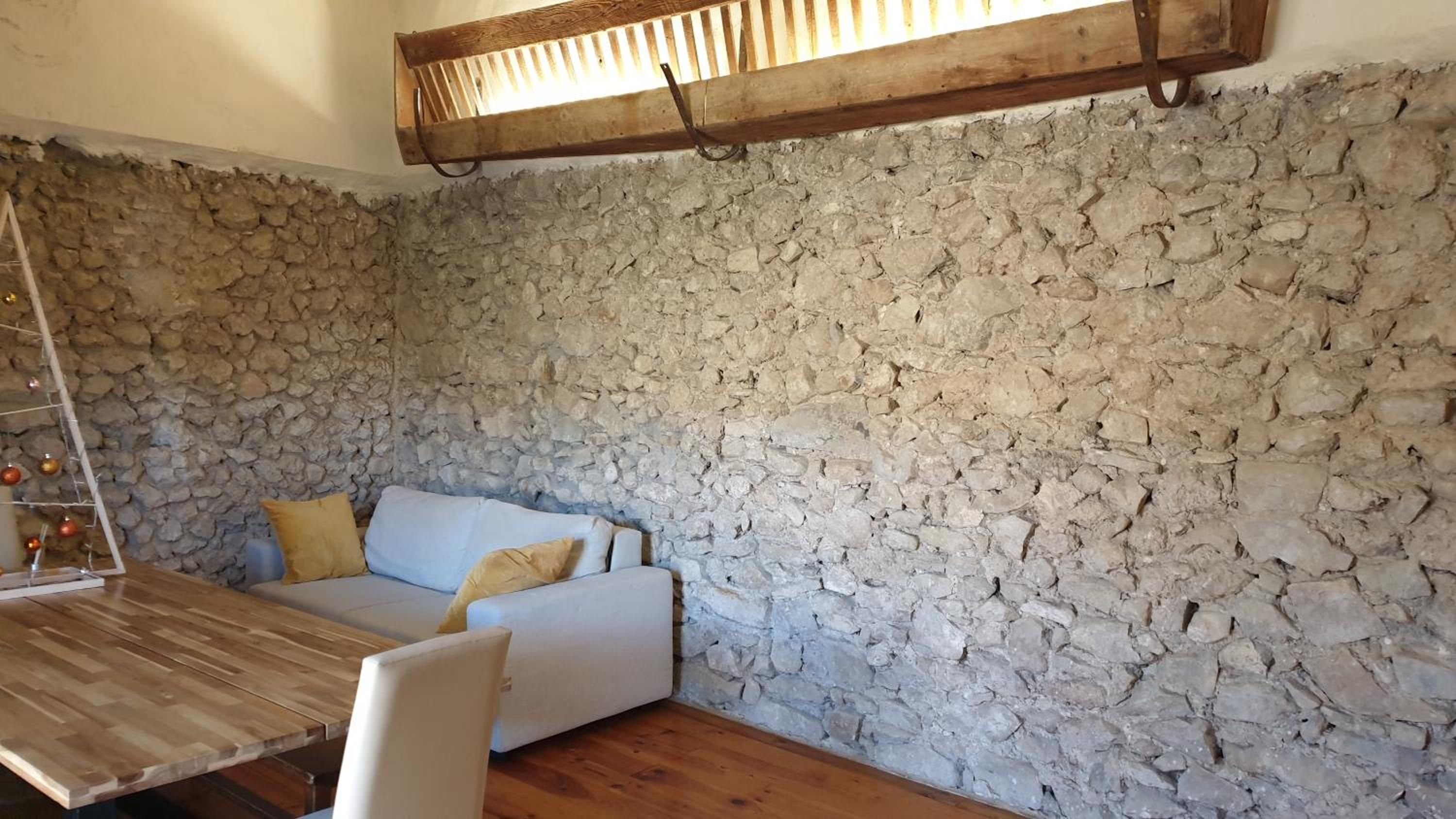Une pièce avec un mur en pierre, un canapé blanc, une table en bois et un luminaire suspendu.