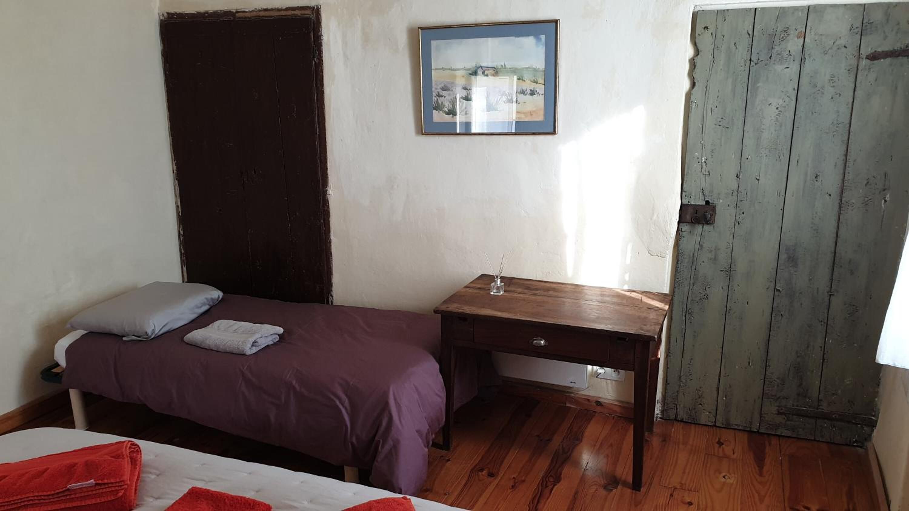 Una habitación con una cama, un escritorio de madera, una puerta y un cuadro en la pared.