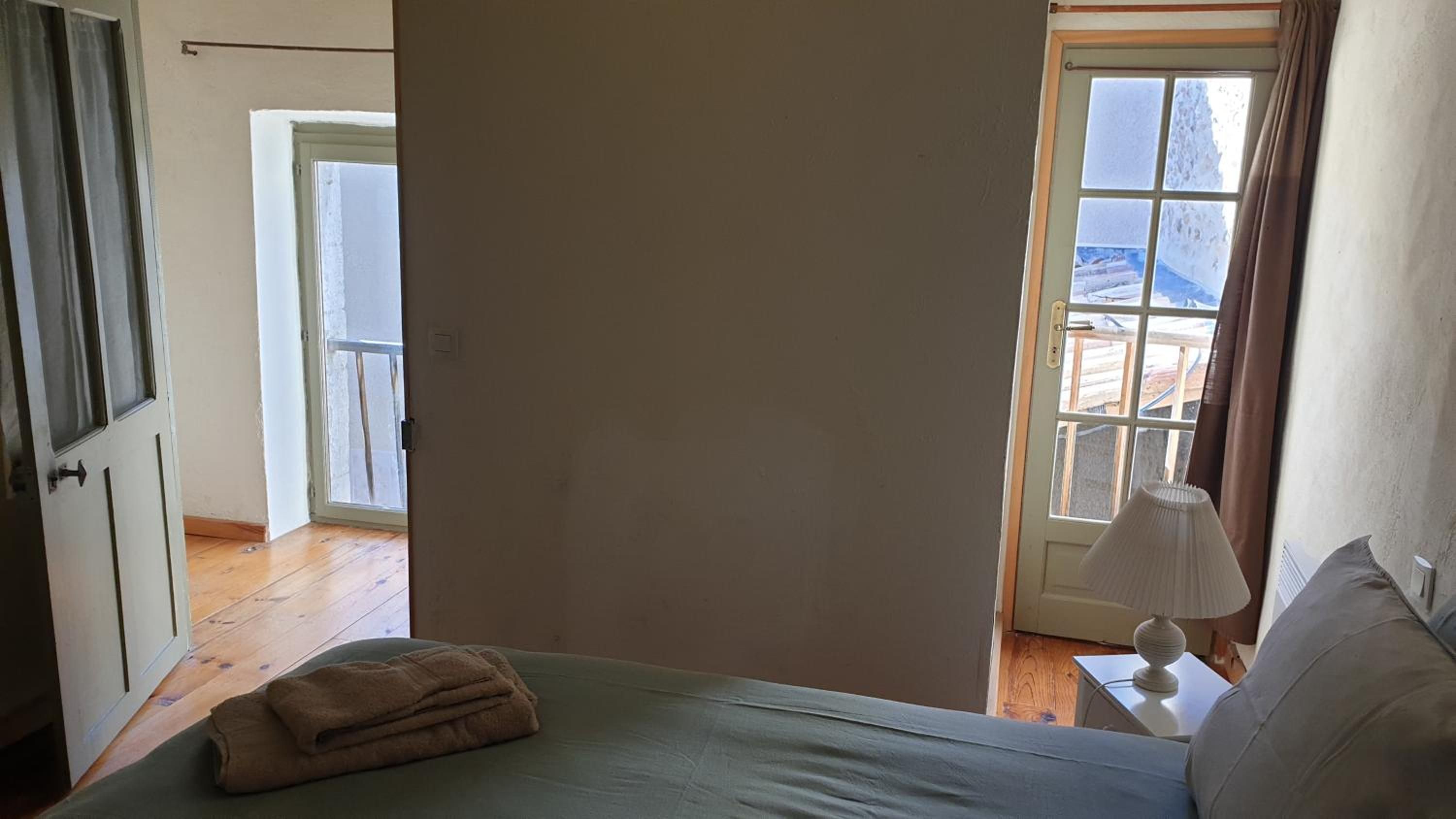 Un dormitorio con cama, ventana con cortinas y puerta que da a otra habitación.
