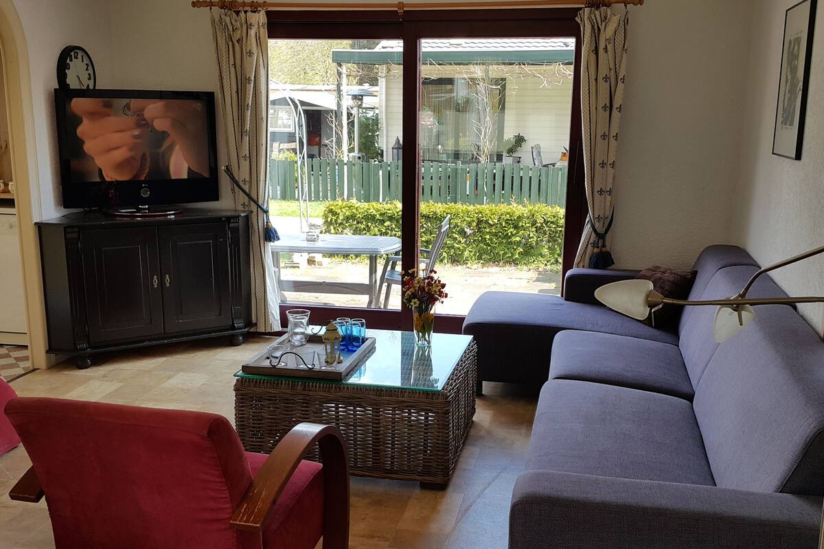 A living room with a television, a sofa, a red chair, a glass coffee table, and a wicker side table.
