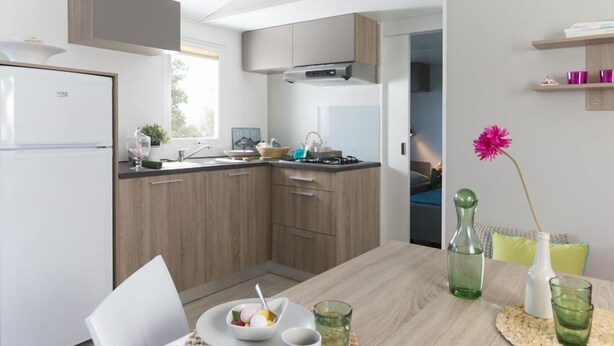 A modern kitchen with wooden cabinets, a built-in stove, and a dining area with a table and chairs. - Fortduinen Campsite (Cromvoirt)