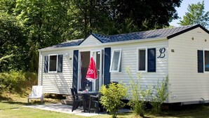A mobile home with a covered patio, a dining table, and a red umbrella. - Fortduinen Campsite (Cromvoirt)