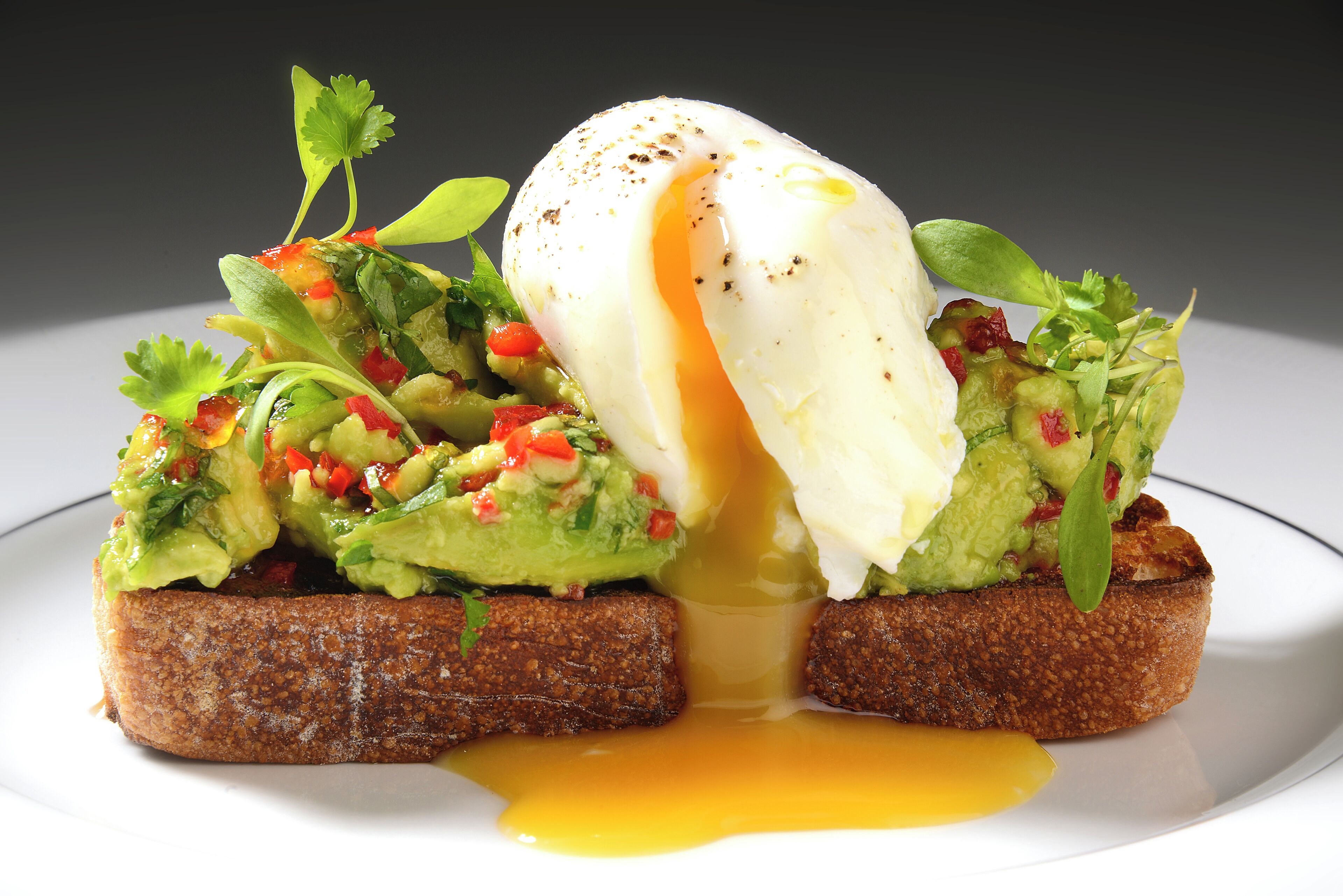 Un plat pour le petit-déjeuner composé d’avocat, d’œuf et de légumes verts, servi sur une tranche de pain grillé.