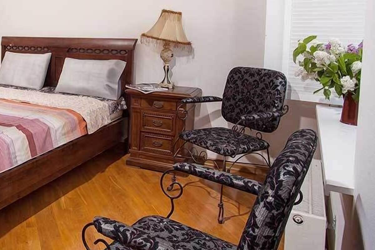 A bedroom with a wooden bed, bedside tables, a chair, and a mirror.