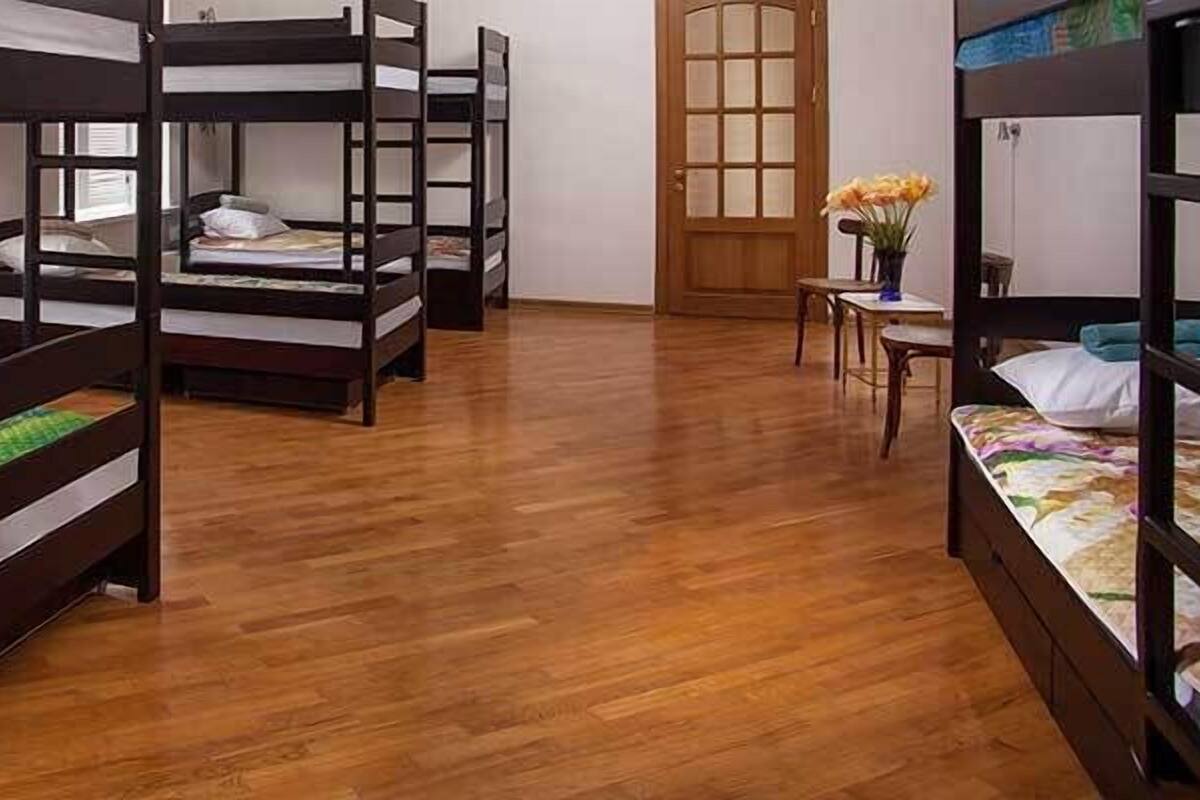 A room with bunk beds, wooden flooring, a window with blinds, and a door with a frosted glass panel.