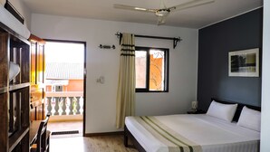 A bedroom with a bed, a ceiling fan, a window with curtains, and a view of the outside balcony. - Hotel H1 Manakara SCHM (Manakara)