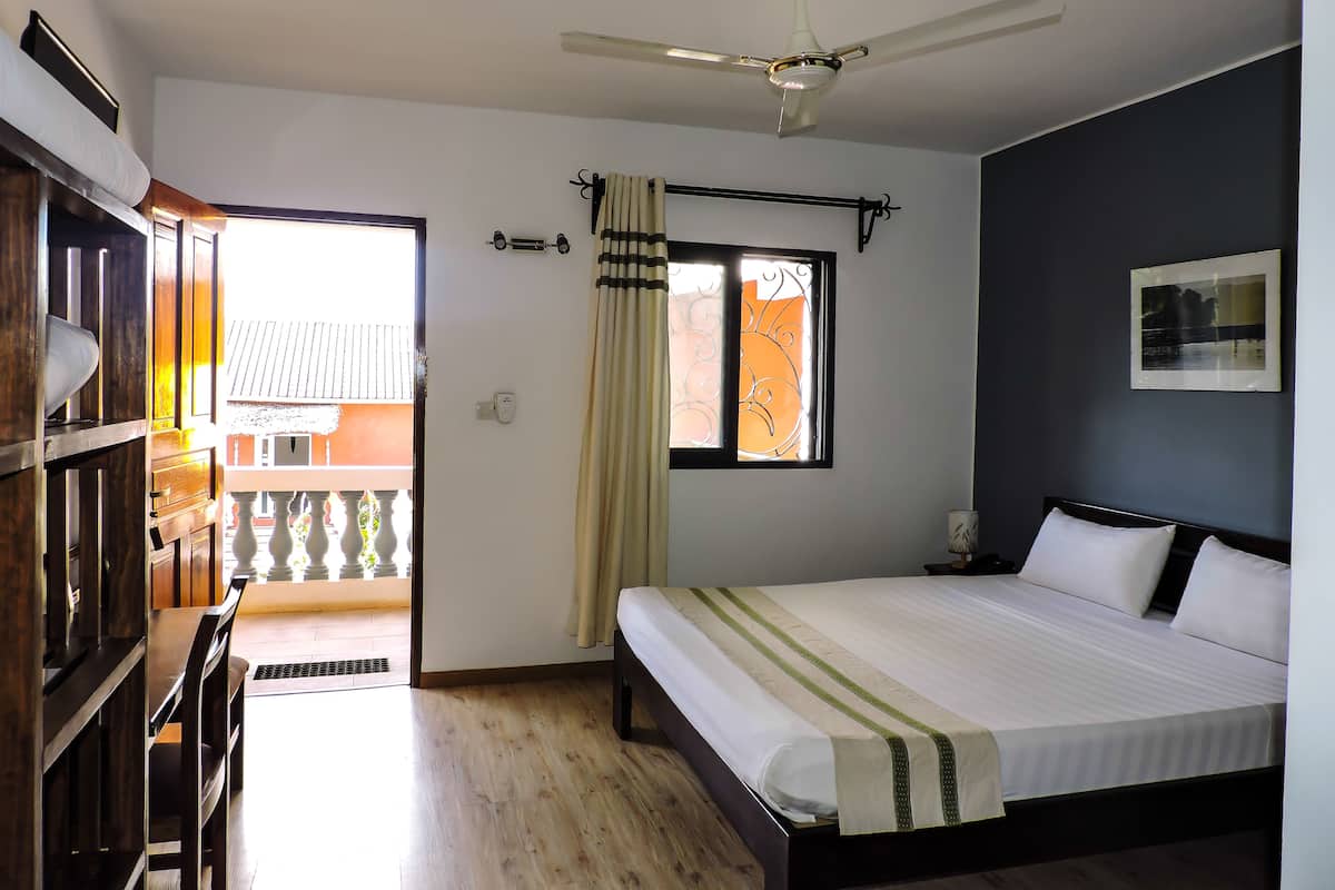 Une chambre à coucher avec un lit, un ventilateur de plafond, une fenêtre avec des rideaux et une vue sur le balcon extérieur.