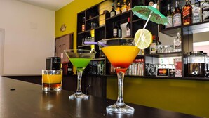 Three cocktails on a bar counter with a shelf of liquor bottles in the background. - Hotel H1 Manakara SCHM (Manakara)