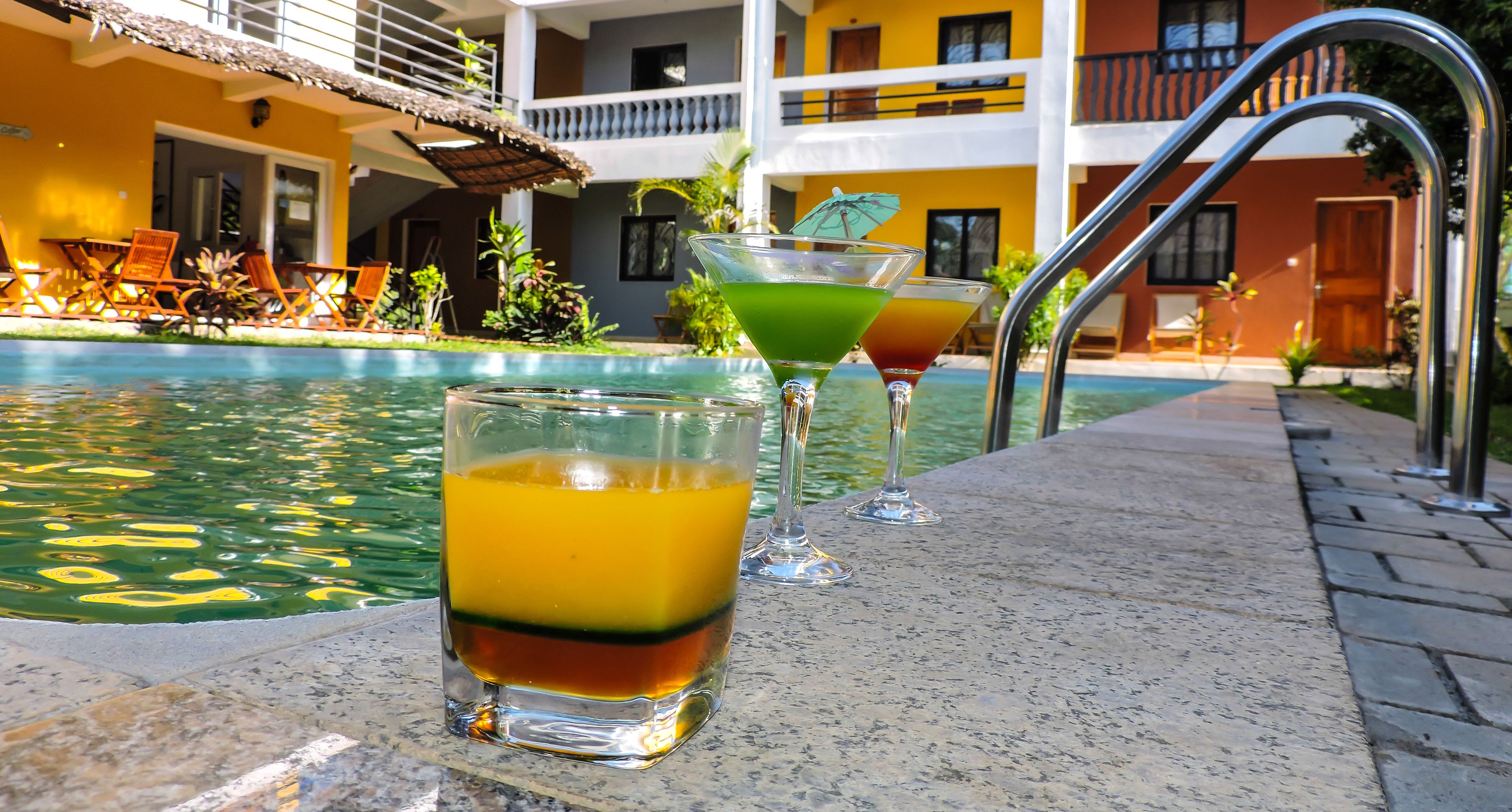 Zona de piscina con sillones reclinables y barra con vasos de bebidas.