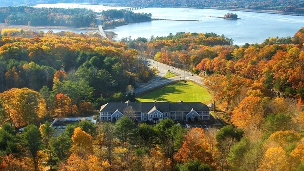 A large house surrounded by autumn foliage, a bridge, and a body of water.