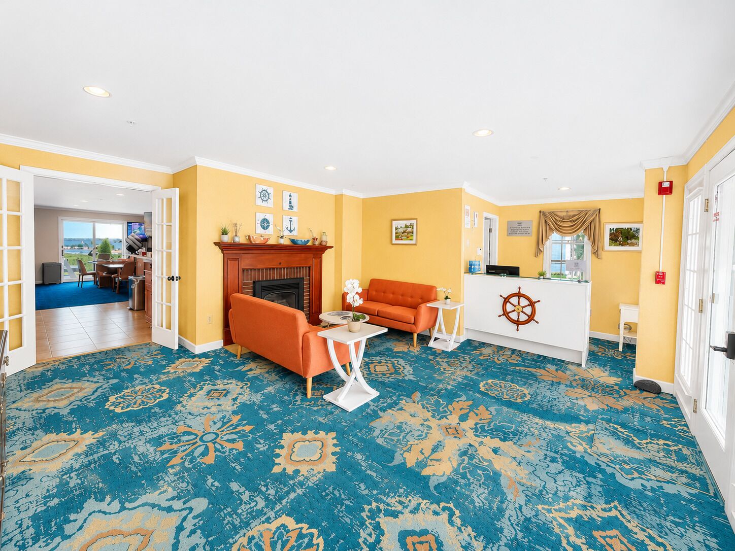 A hotel lobby with a fireplace, orange sofa, and a reception desk with a ship wheel decoration.