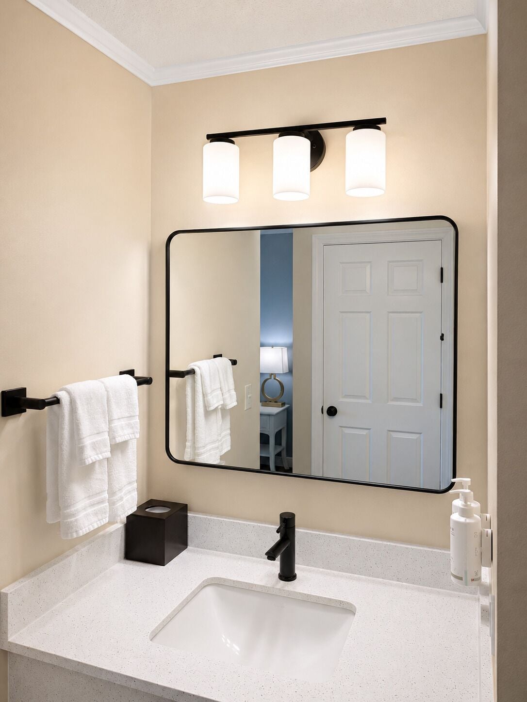 A bathroom with a white sink, black faucet, and a mirror with three lights.