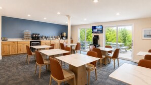A modern dining area with tables and chairs, a kitchen area with appliances, and a TV screen. - Cod Cove Inn, BW Signature Collection (Edgecomb)