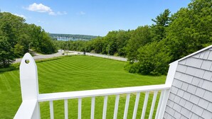 A deck with wicker furniture overlooking a well-maintained lawn and a distant body of water. - Cod Cove Inn, BW Signature Collection (Edgecomb)