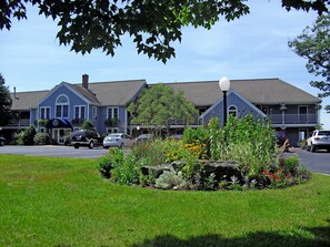 A two-story building with a blue exterior and a white dome on the second floor. There is a garden with various plants and flowers in front of the building.