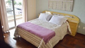 A bedroom with a bed, a nightstand, a window with curtains, and a view of buildings outside.