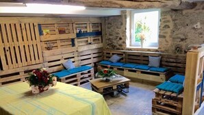 Quarto rústico com bancos de madeira, uma cama, uma pequena mesa e janela com vista para o verde.