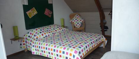 Un dormitorio con cama, una silla, un tablón de anuncios verde y techo de madera.